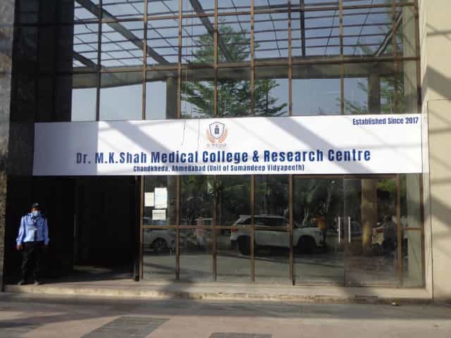 Main entrance of Dr. M.K. Shah Medical College & Research Centre, Chandkheda, Ahmedabad, with a signboard reading 'Established Since 2017' and 'Unit of Sumandeep Vidyapeeth'