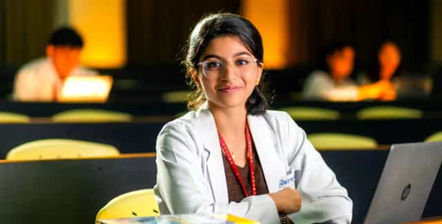 MBBS student wearing a KSHEMA lanyard seated in a tiered lecture theatre at K S Hegde Medical Academy, Mangalore