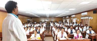 A faculty member addressing MBBS students in white coats in a wood-panelled lecture hall at Bhaarat Medical College & Hospital, Chennai