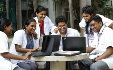 Medical students in white coats at a group study table on the Chettinad Health City campus, Kelambakkam