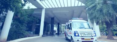 Portico entrance of the attached Dhanalakshmi Srinivasan Hospital with a Tamil Nadu ambulance parked outside