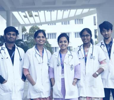 Group of MBBS students in white coats with stethoscopes in front of the college building at Dhanalakshmi Srinivasan Medical College