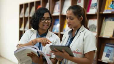 Two students in Dr. Patnam Mahender Reddy Institute of Medical Sciences white coats reading in the central library
