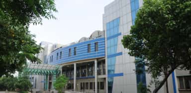 Side view of the G. K. General Hospital teaching block at GAIMS Bhuj, framed by trees