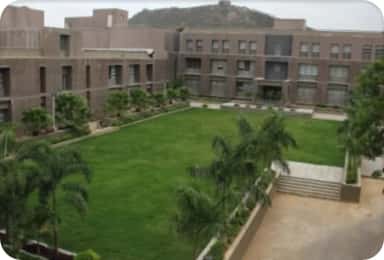 GAIMS Bhuj academic blocks around a green lawn with the Bhujia hill rising behind the campus