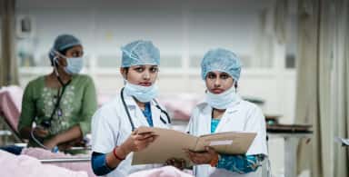 Medical staff in caps and masks reviewing an outpatient record inside a ward of Justice K S Hegde Charitable Hospital, the teaching hospital of K S Hegde Medical Academy