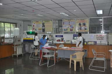 Staff in the hospital biochemistry laboratory with analysers and department banners at Meenakshi Medical College, Kanchipuram