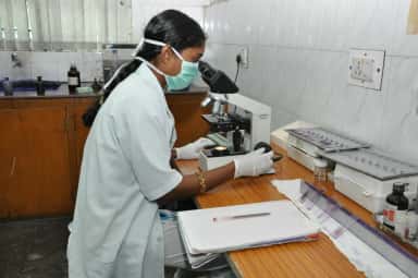 Technician examining a slide under a microscope in the pathology laboratory of Meenakshi Medical College, Kanchipuram