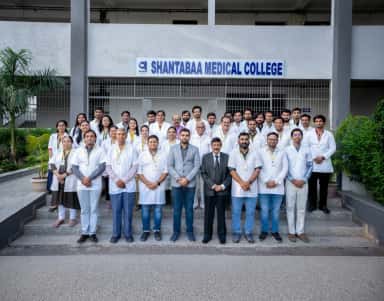 Faculty members of Shantabaa Medical College outside the building under the college name signage, Amreli