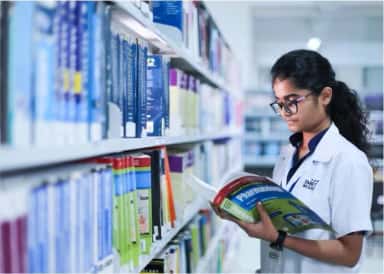 Student reading a pharmacology textbook between book stacks in the central library at SMBT Institute of Medical Sciences
