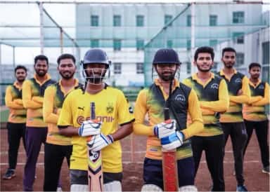 Students in cricket kit on the sports ground of the SMBT Nandi Hills campus with college buildings behind