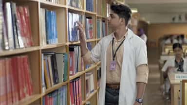 Medical student in a white coat browsing textbooks in the Sree Balaji Medical College central library