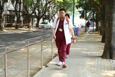 Student in a white coat on the paved walkway of the Sri Devaraj Urs Medical College campus