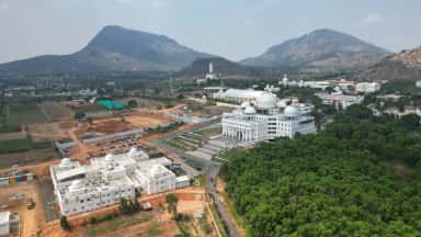 Wide aerial of Sathya Sai Grama, Muddenahalli, showing the SMSIMSR campus buildings amid the Nandi hills landscape