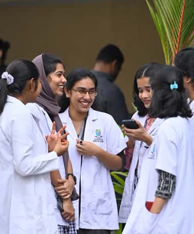 Yenepoya Medical College students in white coats chatting outdoors on the Deralakatte campus