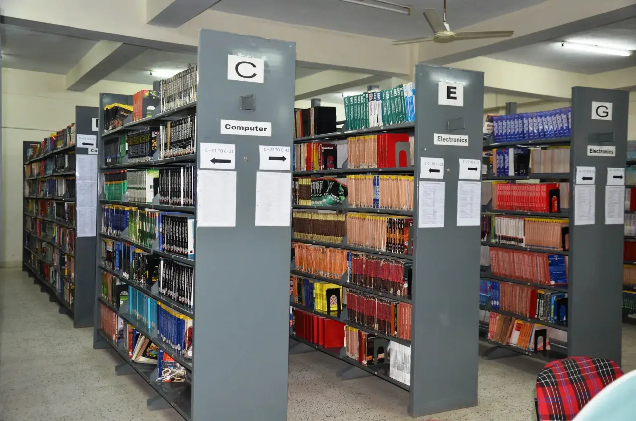 Library aisles with tall gray shelves labeled C and E, packed with colorful books. — Arya College of Engineering & Research Centre
