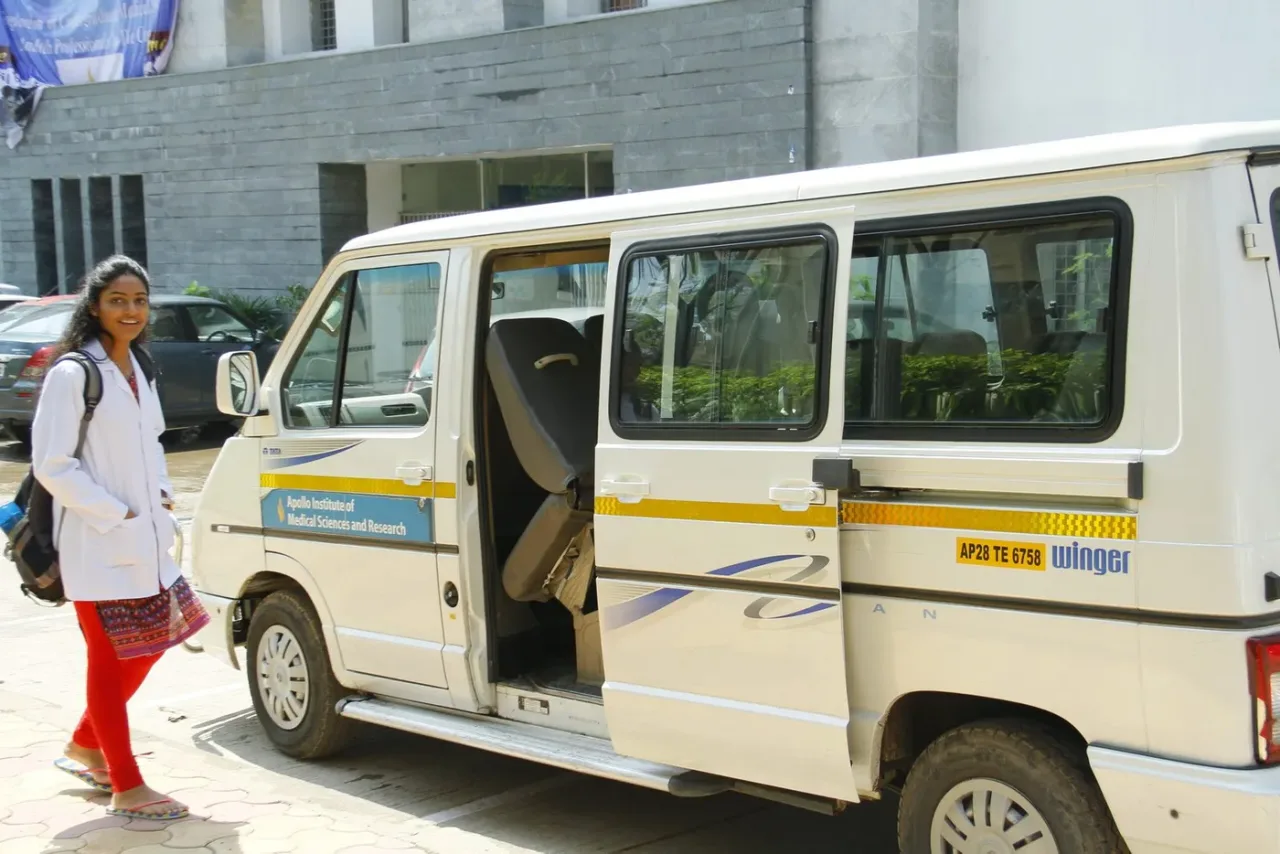 MBBS student in a white coat beside the Apollo Institute of Medical Sciences and Research college vehicle on campus