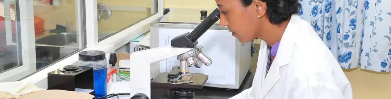 Laboratory technologist using a microscope in a clinical laboratory at Srinivas Hospital, Mukka