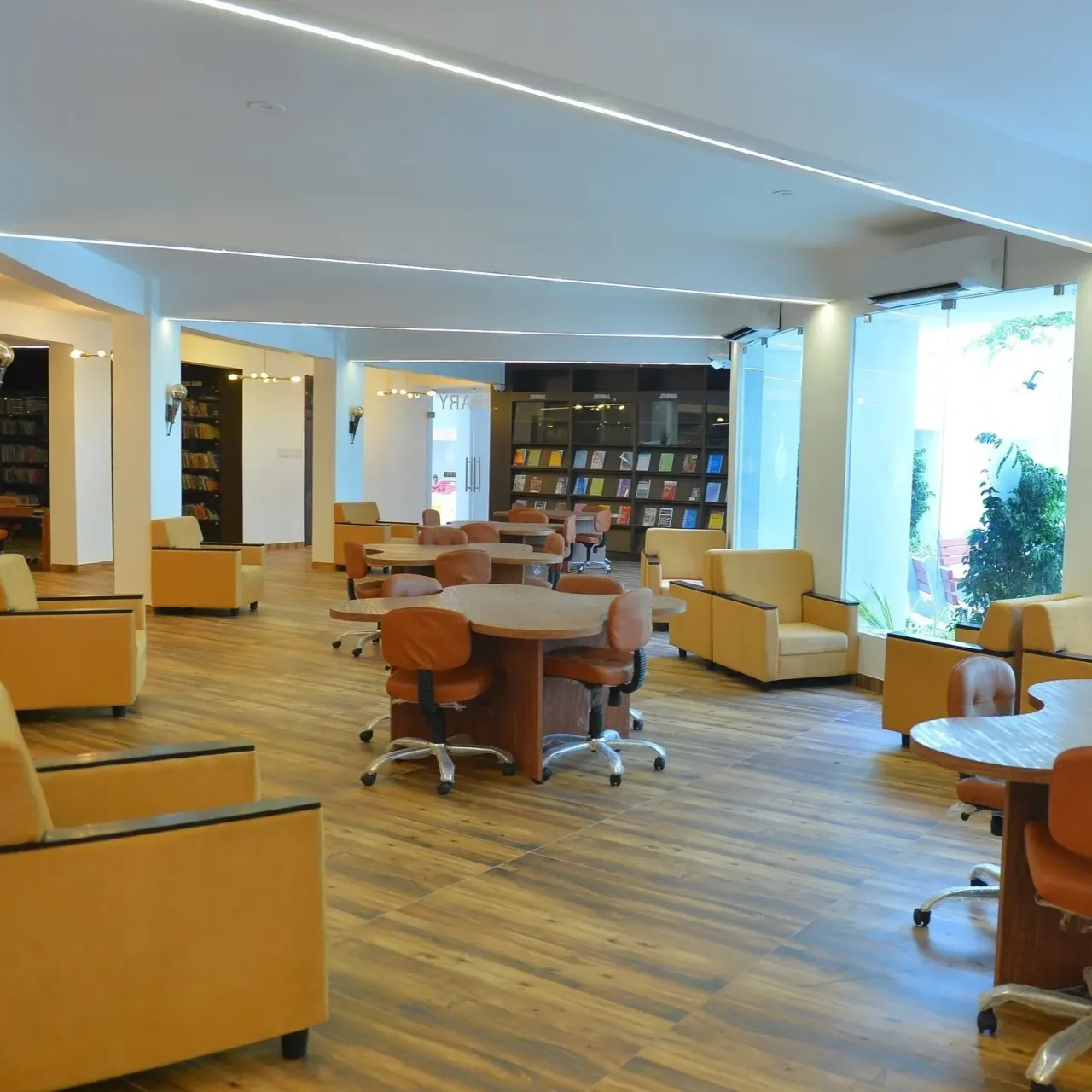Modern library reading area with bookshelves, tables and lounge seating — Saveetha College of Nursing