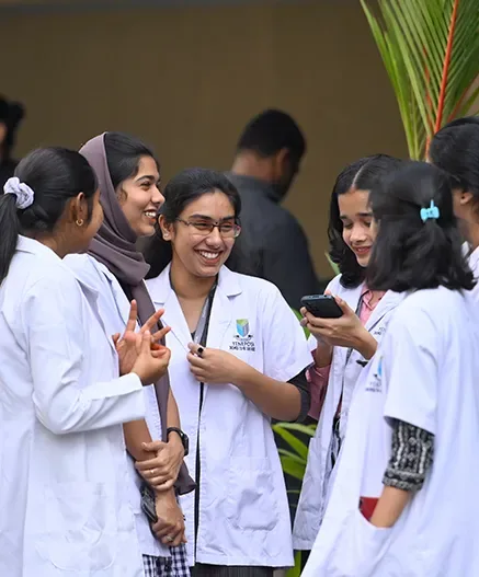 Yenepoya Medical College students in white coats chatting outdoors on the Deralakatte campus