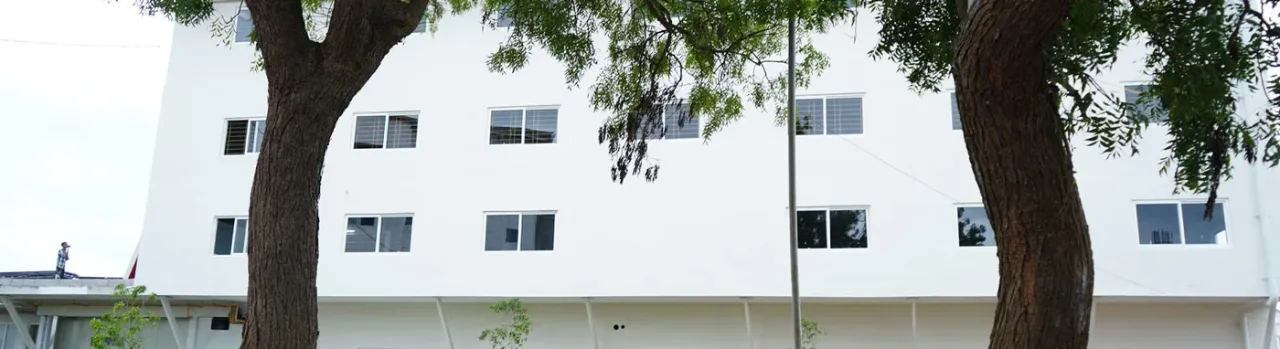 White campus block of Farookh Academy of Medical Education seen through trees