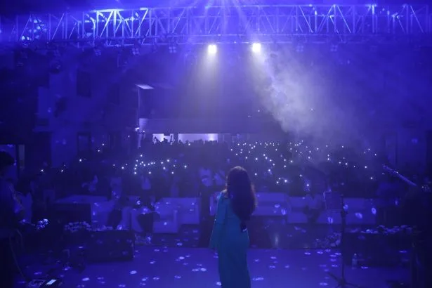 Singer in a blue dress on stage facing a packed audience under blue lights. — Christian College of Law