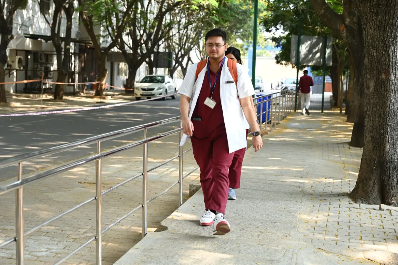 Student in a white coat on the paved walkway of the Sri Devaraj Urs Medical College campus