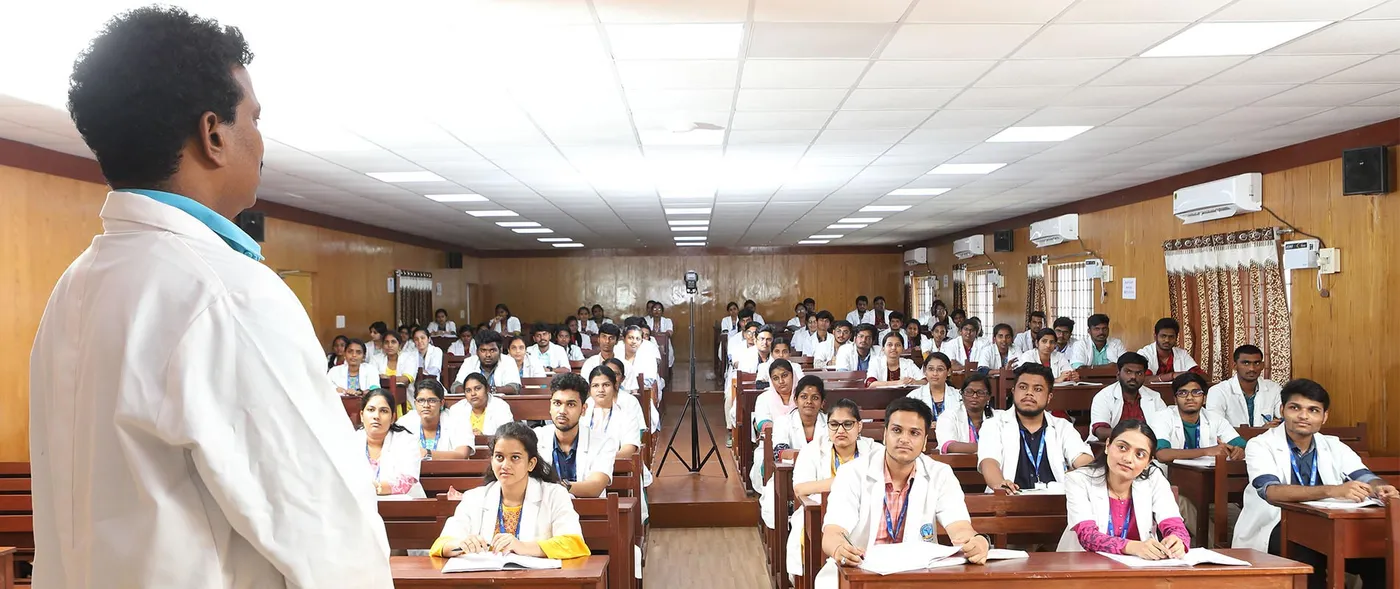 A faculty member addressing MBBS students in white coats in a wood-panelled lecture hall at Bhaarat Medical College & Hospital, Chennai