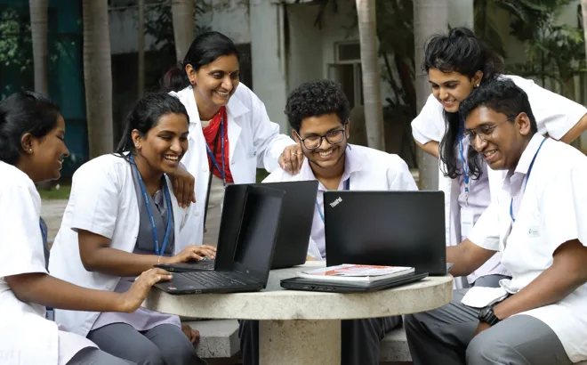 Medical students in white coats at a group study table on the Chettinad Health City campus, Kelambakkam