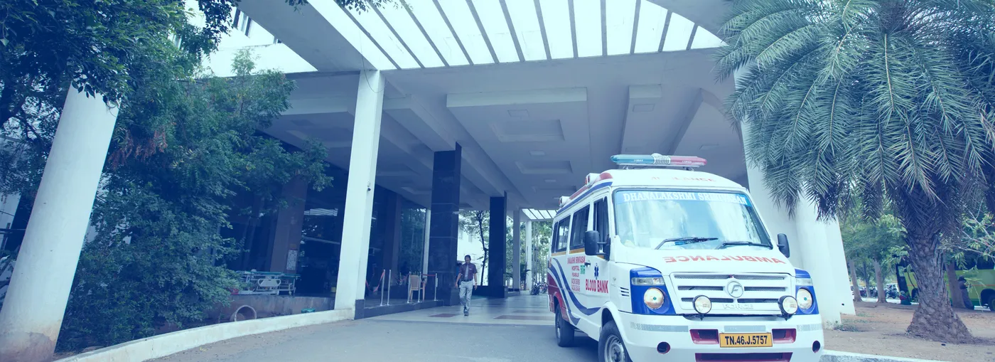 Portico entrance of the attached Dhanalakshmi Srinivasan Hospital with a Tamil Nadu ambulance parked outside