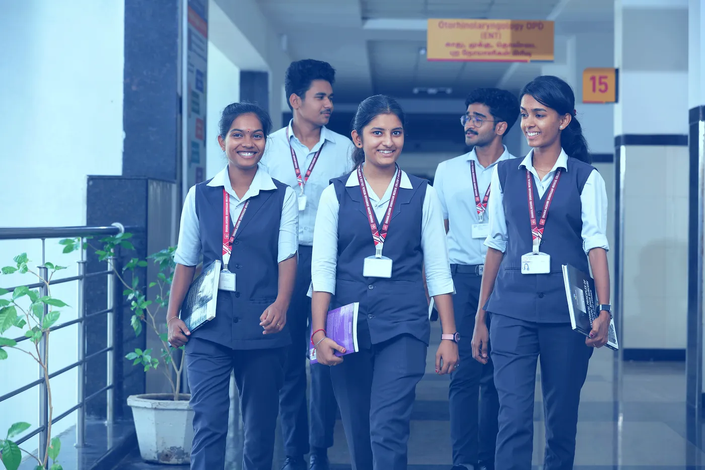 Students of Dhanalakshmi Srinivasan Medical College in uniform with ID lanyards walking through a campus corridor
